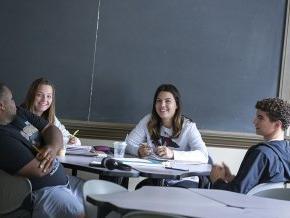 Four students study together around a table in front of a chalkboard